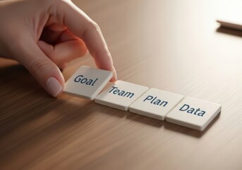 Hand arranging tiles with goal, team, plan, and data on wooden table
