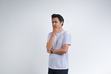 A young man in a white t-shirt standing with a thoughtful expression, and looking away as if deep in thought, isolated on plain background.