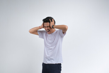 Fototapeta premium A young man in a white t-shirt with a frustrated and stressed expression. Studio shot on plain background showing human emotion.