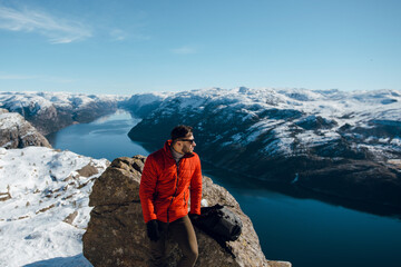 Naklejka premium Young travelling man sitting on rock and enjoying scenic landscape of fjord