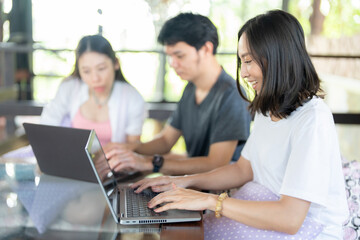 A Group of 3 Asian students spends their afternoon in the university library, tutoring classmates, reading detailed notes, and relying on a laptop to practice quizzes and online lessons.