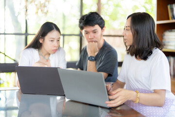 Fototapeta premium In preparation for tomorrow, 3 Asian students work on a project with a laptop, balancing education goals and industry knowledge to strengthen their readiness for the future.