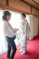 Obraz premium A woman in a kimono is being helped by another woman. The woman in the kimono is wearing a white shirt and black pants