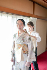 Fototapeta premium A woman in a kimono is being helped by another woman. The woman in the kimono is wearing a white shirt underneath her kimono