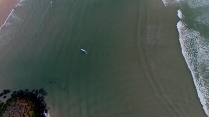 aerial view of a surfer floating in tranquil sea near sandy beach and gentle wave