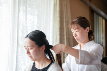 Fototapeta premium A woman is getting her hair done by another woman. The woman getting her hair done is wearing a black shirt and a white jacket