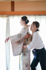 Obraz premium A woman is getting her dress altered by another woman. The dress is a traditional Japanese kimono. The two women are standing in a room with a window