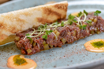 veal tartare with microgreens in a plate of bruschetta macro photo