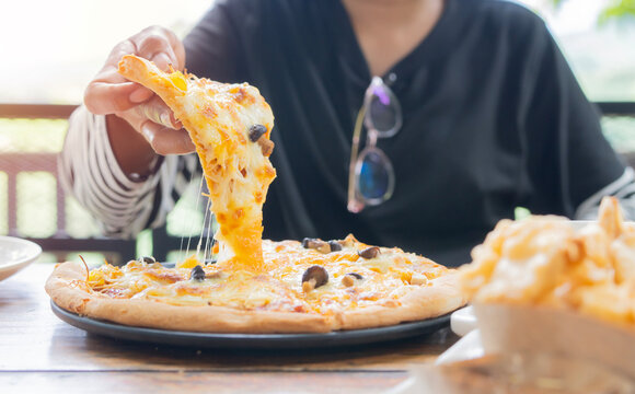 Close up of woman enjoying meal and eating freshly made pizza in a restaurant - Powered by Adobe
