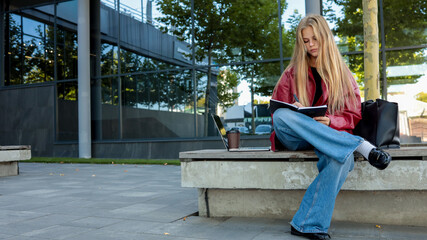 A blonde student sits on a bench outside, writing in her notebook.