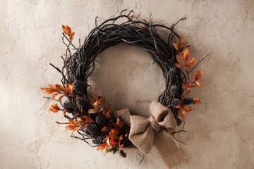 Fototapeta premium A rustic, autumnal wreath with dark branches, warm orange accents, and a burlap bow, hangs beautifully on a textured wall.