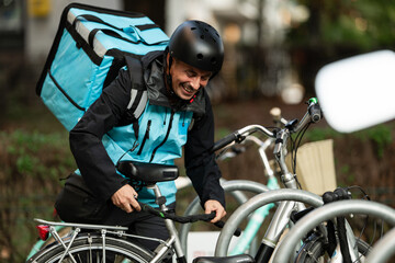 Smiling delivery man locking bicycle in urban setting