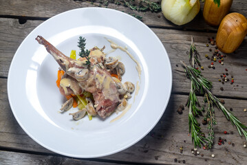 fried rabbit leg in creamy sauce in a white plate on a wooden background with decor