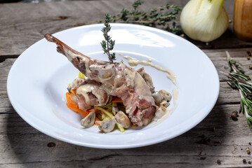 fried rabbit leg in creamy sauce in a white plate on a wooden background