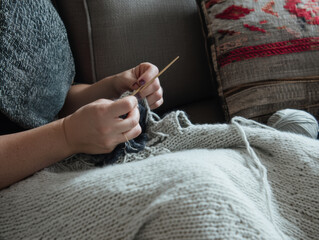 Cozy knitting hands wool yarn on couch blanket