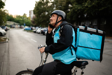 Delivery man using smartphone and riding bicycle on city street