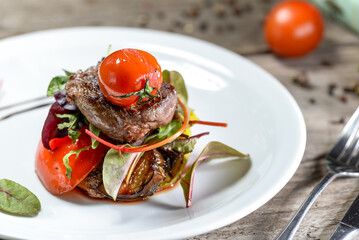 steak with grilled vegetables and tomatoes in a white plate on a wooden background close-up