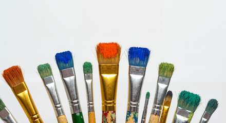 Row of colorful paint brushes with dried acrylic on bristles, gold and silver ferrules, isolated on white background, art supplies banner for creative painting workshop and design mockup, copy space