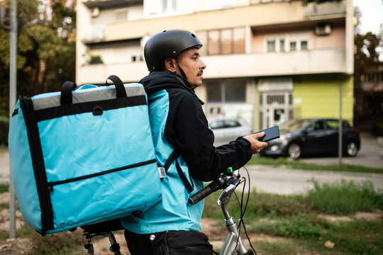 Deliveryman using smartphone and carrying thermal backpack riding bicycle