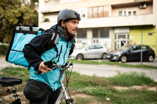 Delivery man pushing bicycle wearing thermal backpack and helmet