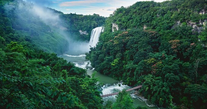Huangguoshu Waterfall in Guizhou Province, China. High angle view of a powerful waterfall cascading down cliff into a misty gorge, surrounded by lush green forest landscape.