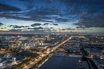 Panoramic view of a large industrial city with a petrochemical complex illuminated at early twilight.