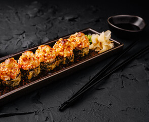 Sushi rolls with shrimp topping served on a dark plate in restaurant setting