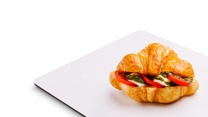Fresh croissant with pesto, tomatoes, and mozzarella served on a plate
