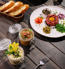 Delicious gourmet meal featuring tartare and assorted spreads on wooden table