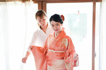 A woman in a pink kimono is being helped by another woman. The scene is set in a room with a...
