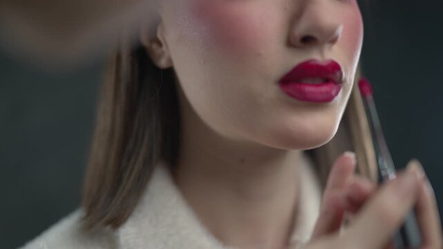 A makeup artist carefully applies red lipstick to a model's lips, enhancing her beauty during a professional makeup session.