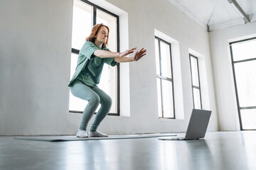 Woman practicing yoga and fitness in a bright indoor space with a laptop