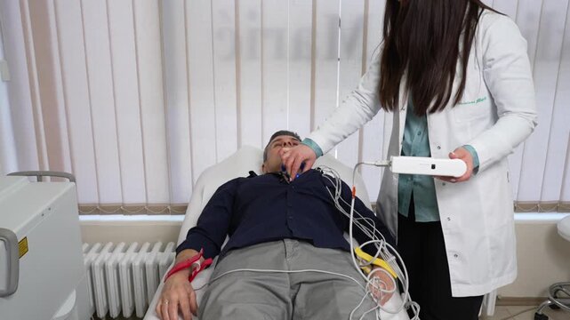 Doctor carefully placing electrodes on the chest of a mature male patient lying on examination table, preparing for an electrocardiogram (ECG) test in a bright medical office