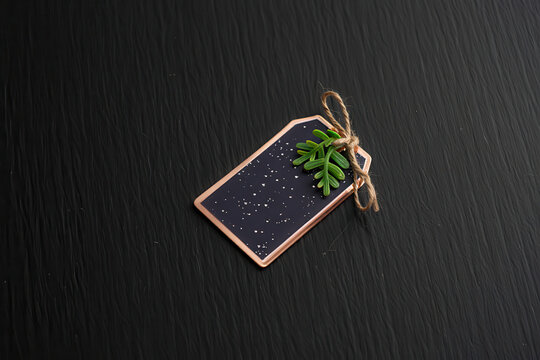 A dark tag with a gold border and a small green decoration on a dark wooden surface texture close up