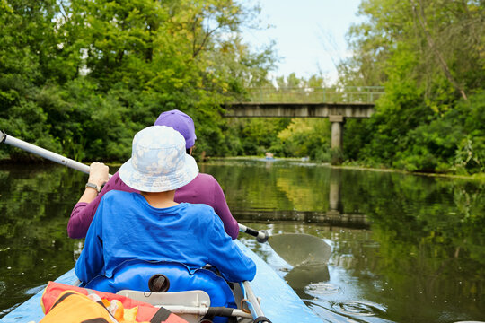 Two people kayaking on a calm river surrounded by green forest. Active outdoor recreation with paddles and nature exploration. Summer adventure on water - Powered by Adobe