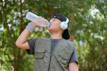 Child wearing headphones drinks water during outdoor activity in a park setting on a sunny day
