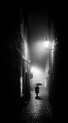 Rainy alleyway with lone figure under umbrella, illuminated by a streetlamp, in stark monochrome