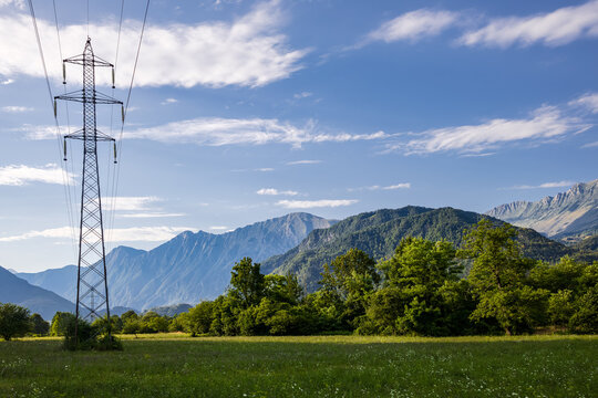 power line on scenic lush green landscape with mountain range and rolling green hills. alpine nature background with power lines