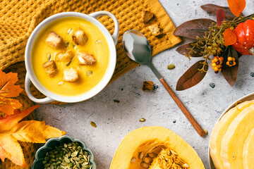 Pumpkin soup with croutons and seeds in bowl on yellow textile, surrounded by autumn leaves, berries, and fresh pumpkin, perfect for fall, Thanksgiving, and seasonal food styling