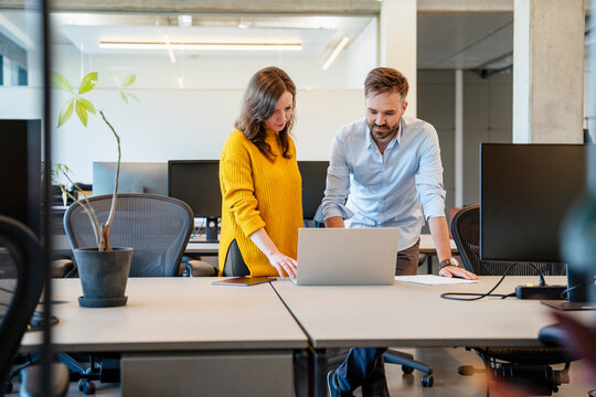 Two colleagues collaborating at laptop in modern office environment