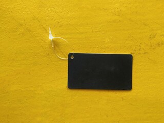 Blank Label on Yellow Surface: A close-up shot of a sleek, dark label hangs suspended against a vivid yellow surface. This simple.