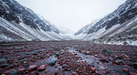 Dramatic mountain landscape with snow-capped peaks and vibrant red river rocks in a valley