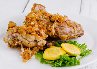 Crispy fried chicken legs lying on white plate with vegetable garnish