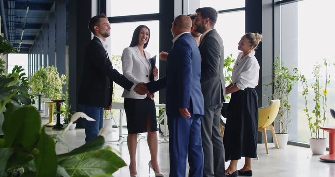 Happy colleagues standing in corporate office hallway to open business meeting with friendly handshake. Team of partners planning project strategy and success collaboration in briefing discussion
