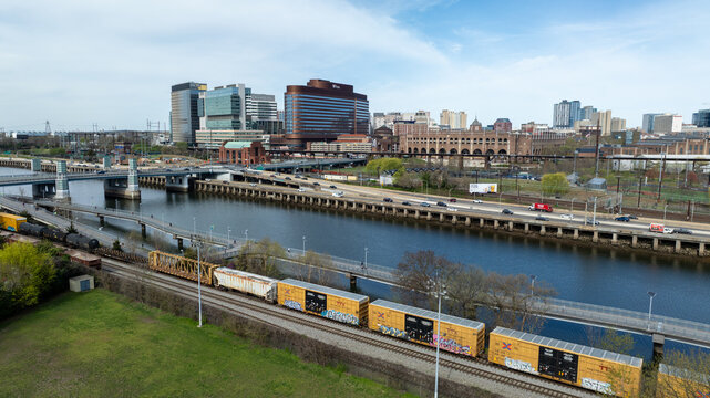 Aerial view of the Schuylkill River snaking through the city's heart, with trains carrying graffiti-covered cargo, set against the backdrop of Philadelphia's skyline, Pennsylvania, United States.