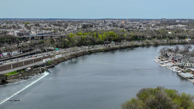 Aerial view of the Schuylkill River reflecting the sky, bordered by lush greenery and the distinctive Boathouse Row, a tapestry of nature and architecture, Philadelphia, Pennsylvania, United States.