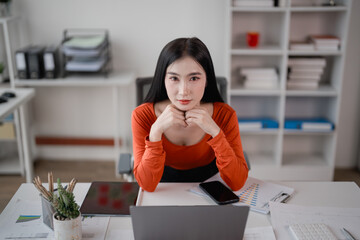 Young asian businesswoman resting her chin on her hands while working with laptop and digital...