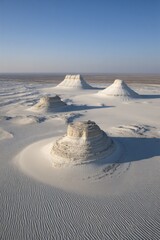 White hills rise from a textured, sandy landscape under a clear blue sky, evoking a serene desert vista with unique geological formations