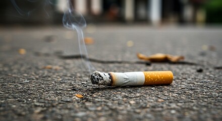 A discarded cigarette smolders on asphalt emitting smoke a leaf lies nearby