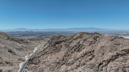 Aerial view of rugged, rocky mountains meet the sprawling cityscape under a vast, clear sky, a stark contrast of nature and urban life, Las Vegas, Nevada, United States.